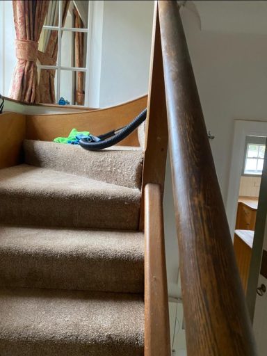 Carpeted staircase with a wooden handrail and a vacuum cleaner resting on the steps.