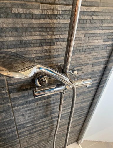 Chrome shower faucet against grey tiled wall.