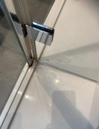 Corner of a glass door with a metal latch and reflections on the floor.