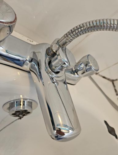 Close-up of a shiny chrome tap with a flexible hose attached.