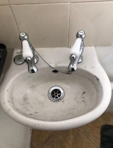 A dirty white bidet with chrome taps, mounted on a tiled wall.