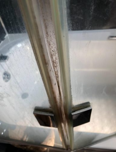 A close-up of a shower screen with water droplets and some dirt along the edge.