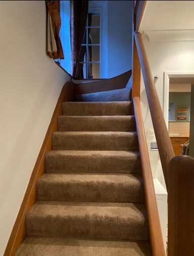 Carpeted staircase leading upwards, with soft lighting and a curtain at the top.