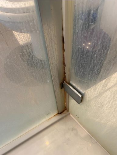 Close-up of a shower door hinge showing rust and moisture damage.