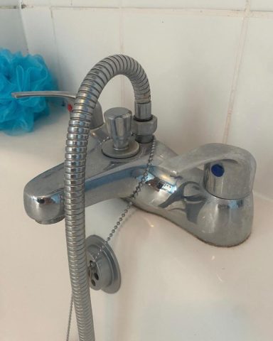 Chrome bath tap with a flexible shower hose and blue bath accessory nearby.