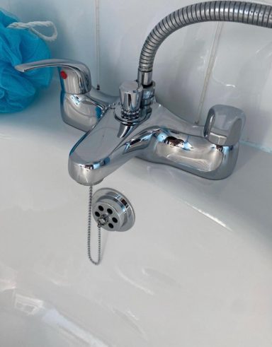 A silver bath tap with a pull-out plug and a flexible hose.