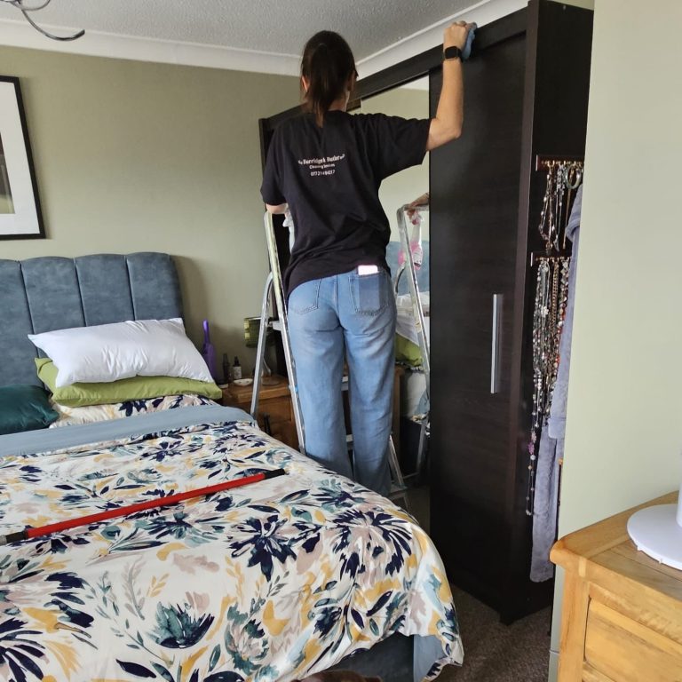 Hayley Person adjusting a wardrobe in a neatly made bedroom with a floral bedspread.