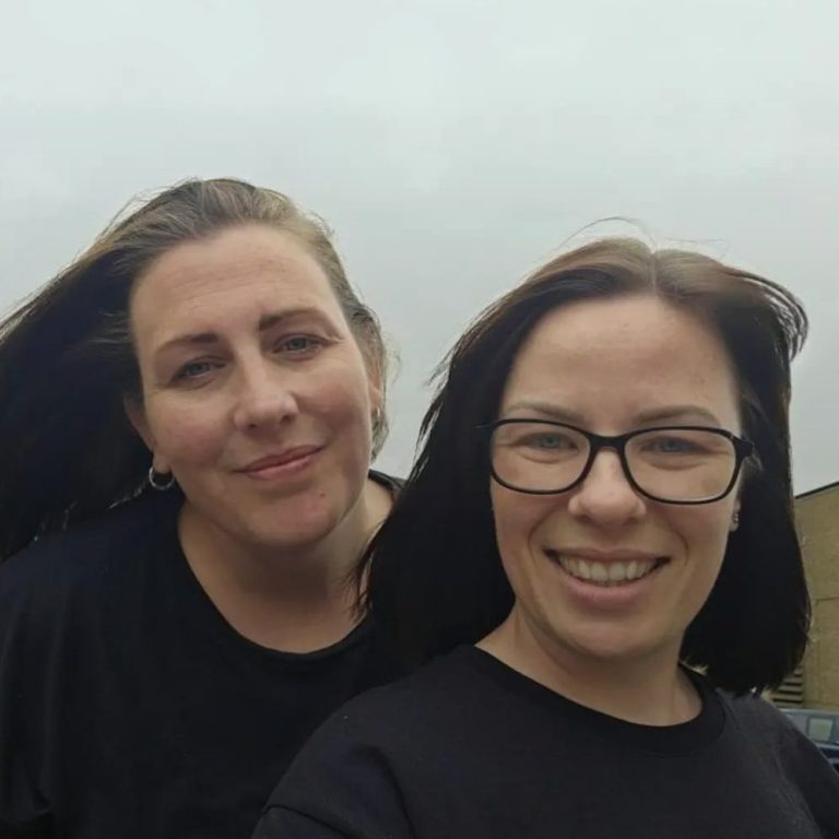 Lauren and Hayley Two women with long hair, smiling and standing close together outdoors.