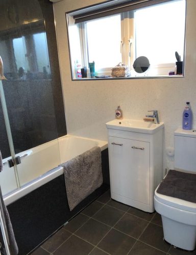 A modern bathroom featuring a bathtub, sink unit, and toilet with window light.